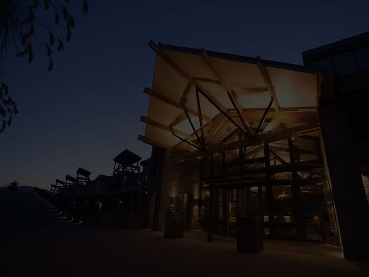 Dark building with large timber canopy over entrance, lit from below, stone cladding at night