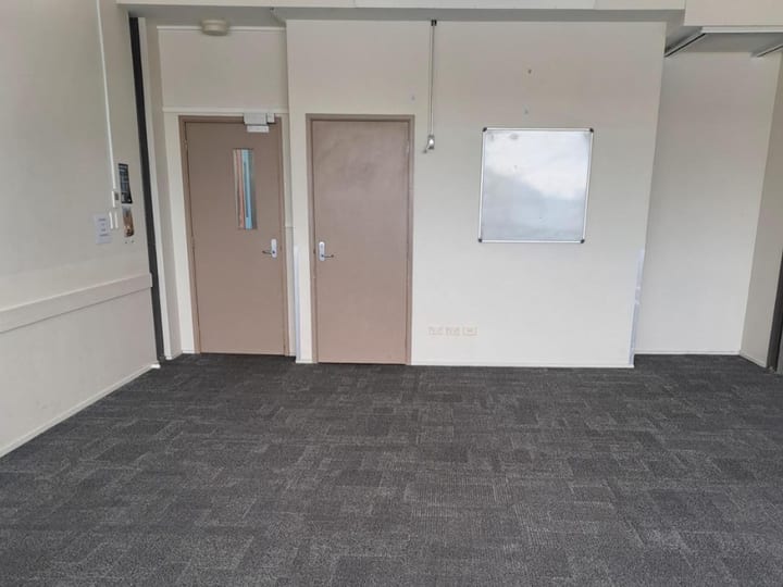 Small empty carpeted meeting room with windows and a whiteboard on a stand