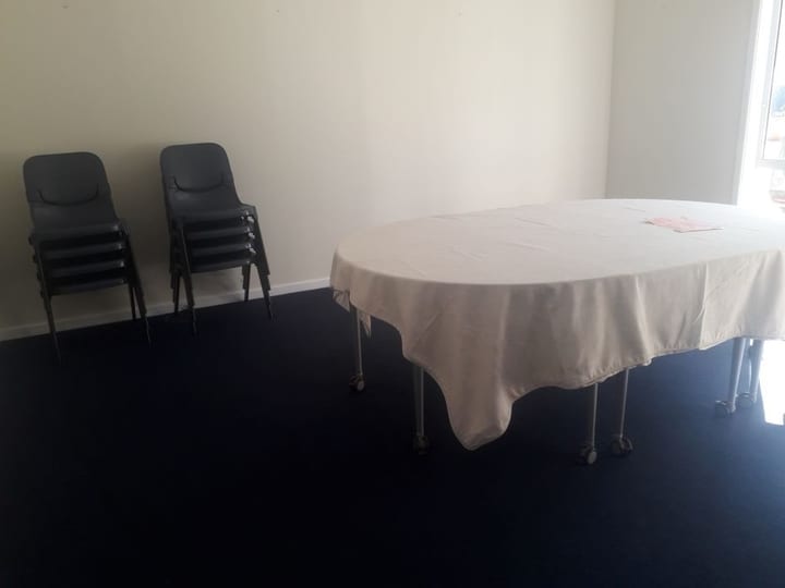 Small room with round draped table and stacked chairs on dark carpet