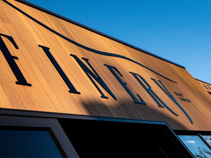 Warm timber-clad barn gable end with large cut-out signage, angular roof, clear blue sky