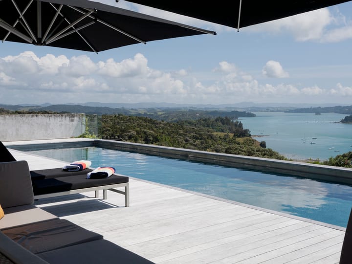 Concrete pool terrace with sun loungers, large shade umbrella, and coastal bay view