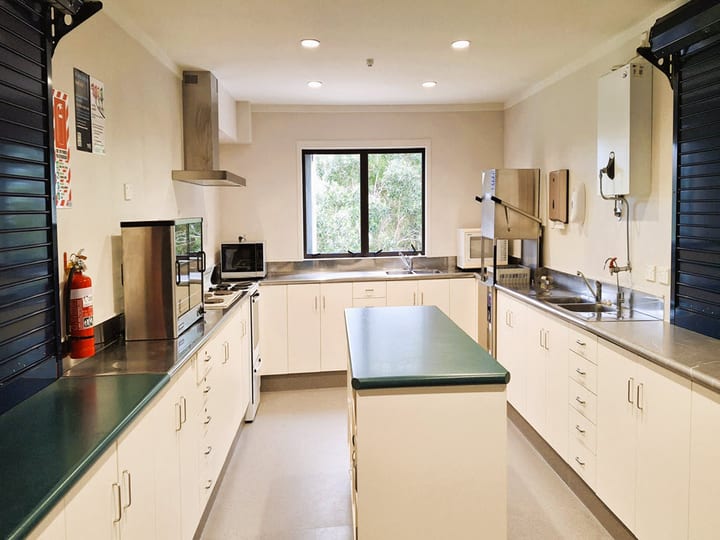 Community kitchen with stainless benches, island, and window to garden