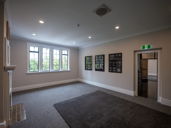 Carpeted room with framed artworks on wall, large windows and doorway to stairwell