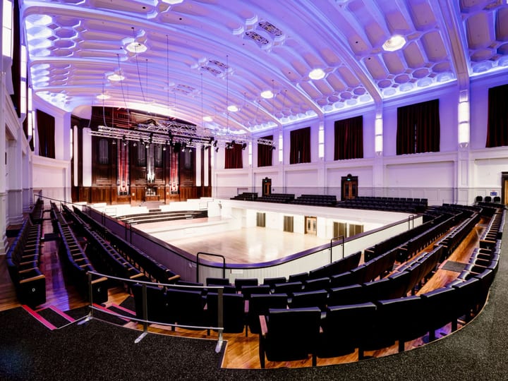 Grand auditorium with tiered seating, ornate white ceiling and pipe organ