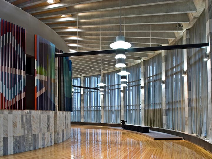 Curved hall with timber floor, marble-clad wall, hanging pendant lights and sheer curtained windows