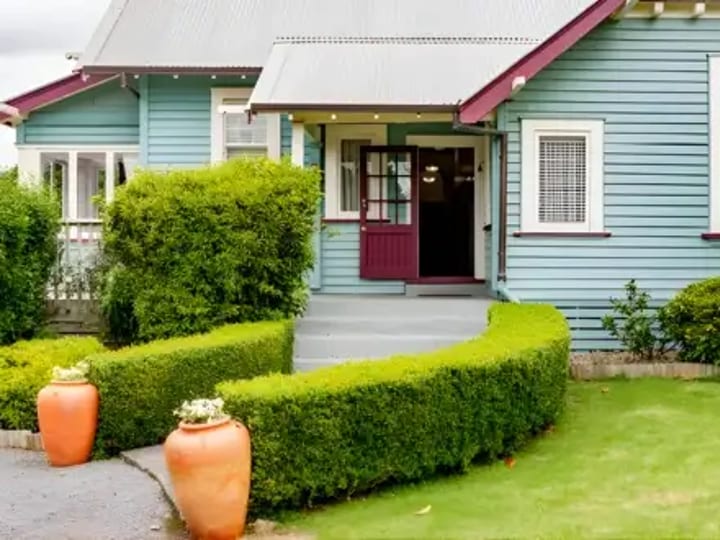 Blue weatherboard villa with hedged front garden and covered entrance