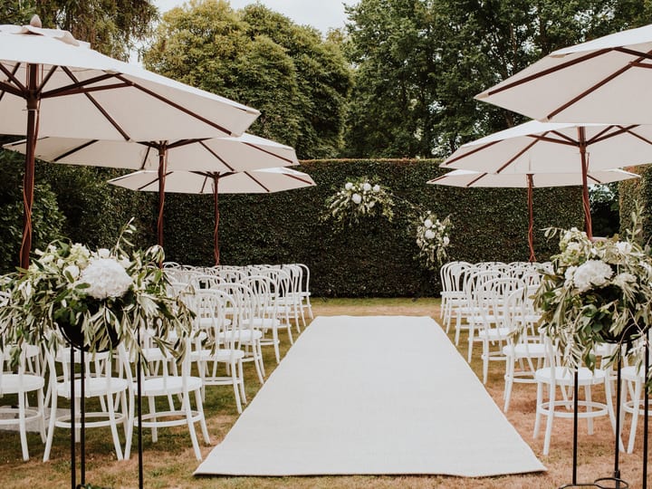 Outdoor ceremony on paved terrace with aisle, white chairs and trimmed hedgerow surrounds