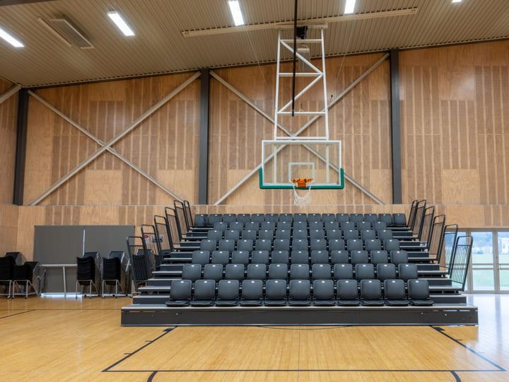 Sports hall with bleacher seating and basketball hoop on timber floor