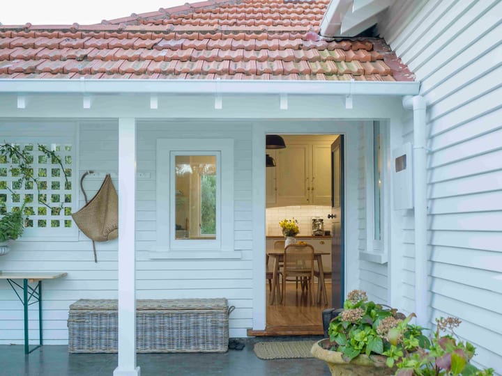 White weatherboard house with covered entry porch, terracotta tile roof and potted plants
