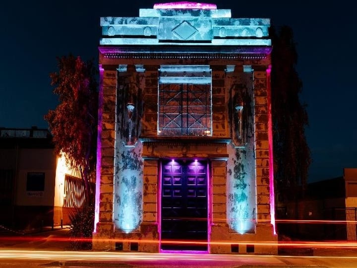 Historic stone building with classical columns lit with coloured lighting at night