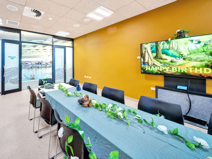 Meeting room with long table, chairs and large display screen on yellow wall