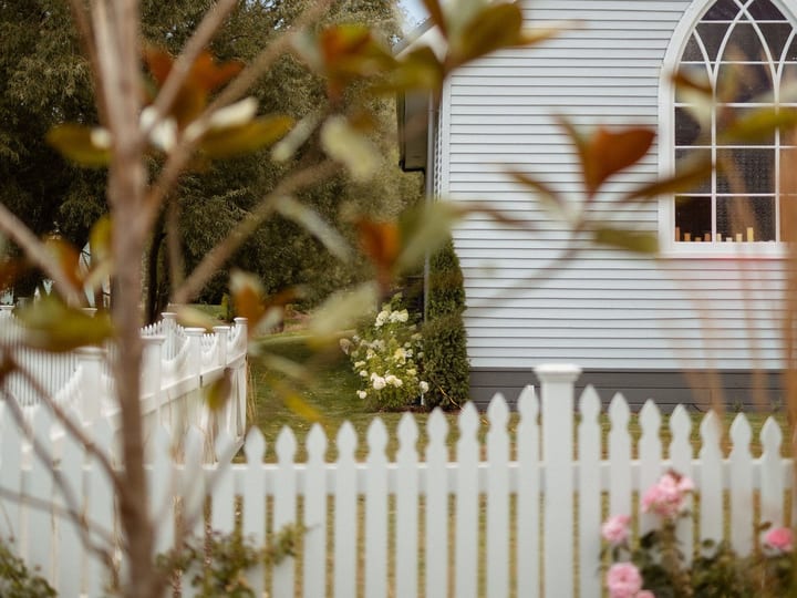 White timber church with Gothic arch window and white picket fence seen through trees