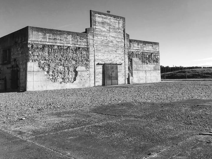 Weathered concrete block building with recessed door, open gravel surrounds
