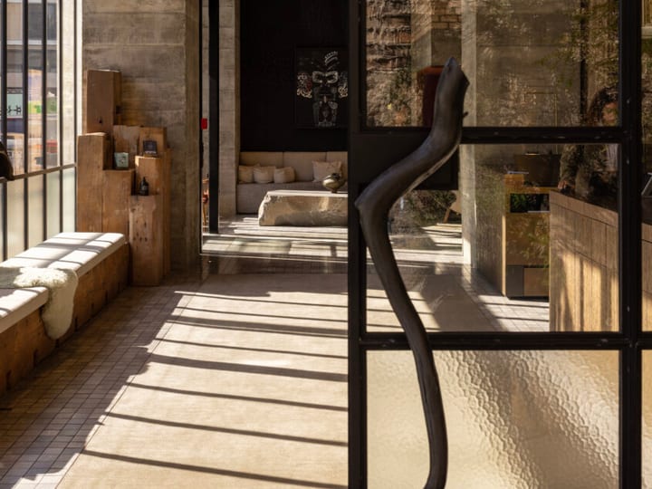 Raw concrete and timber interior with black steel-frame windows, stone bench seating and sculpture