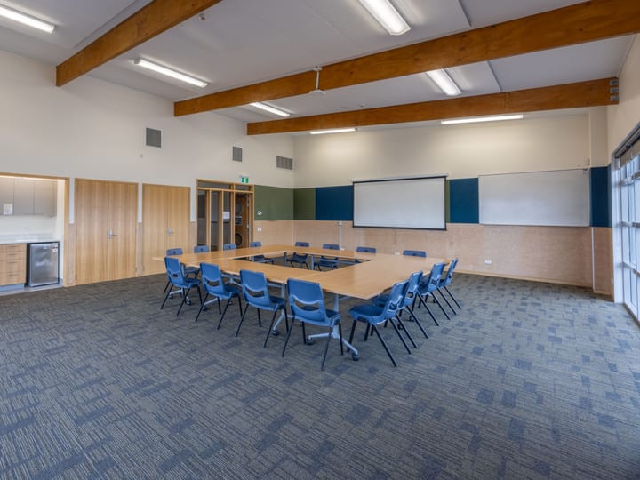 Community hall with exposed timber beams, tables in U-shape arrangement and whiteboard
