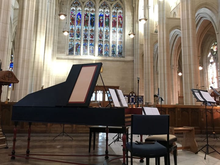 Cathedral nave with arched columns, stained glass windows and a grand piano set up for performance