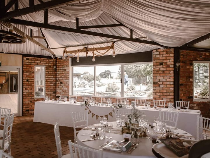 Brick-walled function room with exposed trusses, draped white fabric ceiling, round tables set for dining