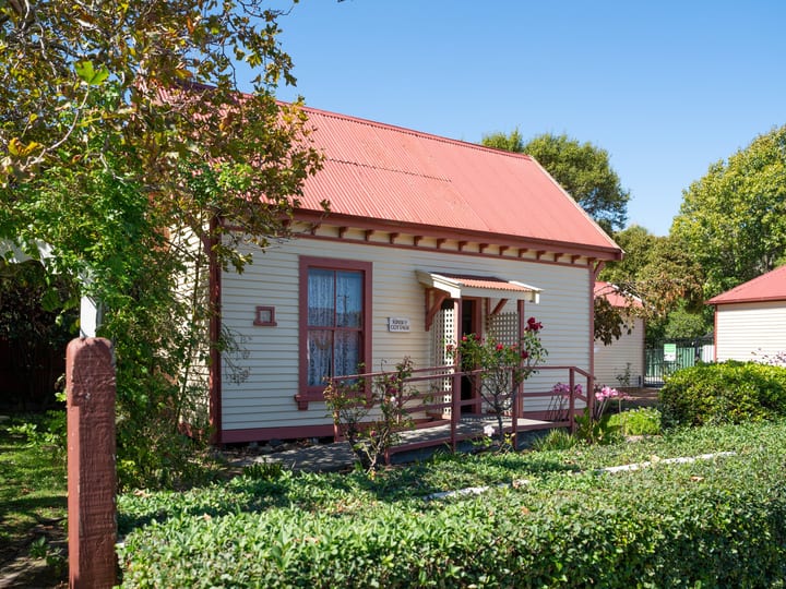 Cream weatherboard cottage with red roof and garden, set in heritage precinct