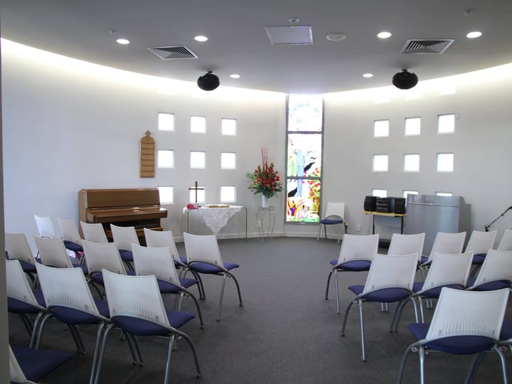 Oval chapel with curved walls, stained glass window and white seating