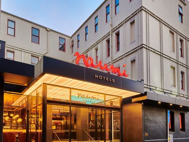 Cream multi-storey building with black canopy entrance, neon signage, street setting at dusk