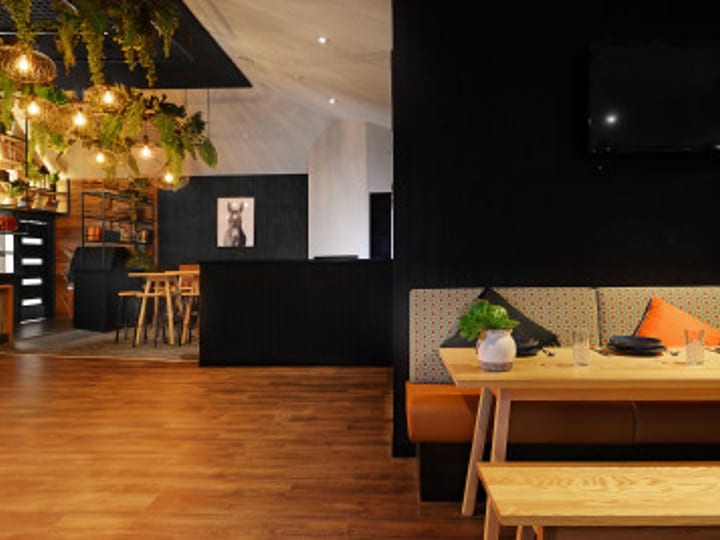 Bar interior with bench seating and pendant lights, viewed from rear