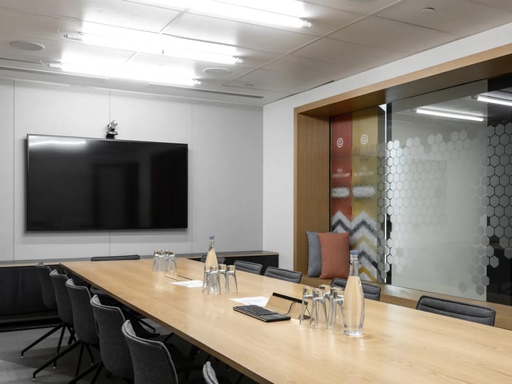 Boardroom with long timber table, chairs, large screen, and patterned glass partition