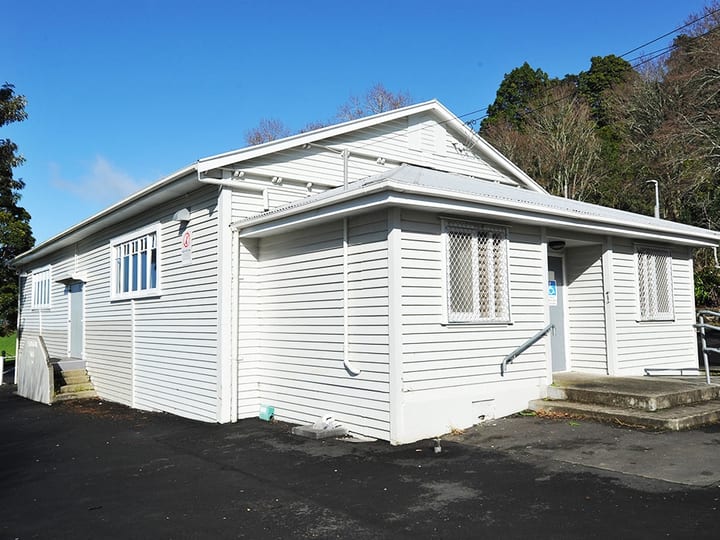 White-painted weatherboard hall building with steps and trees behind