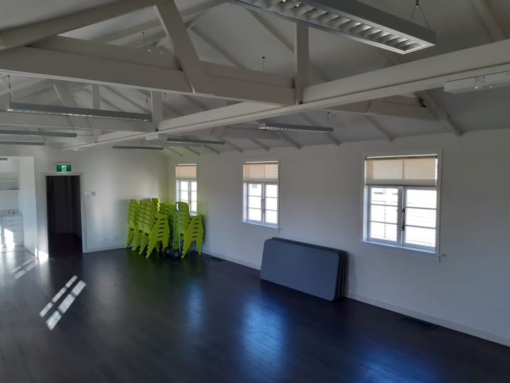 Empty hall with exposed timber roof trusses, stacked lime green chairs and dark floor