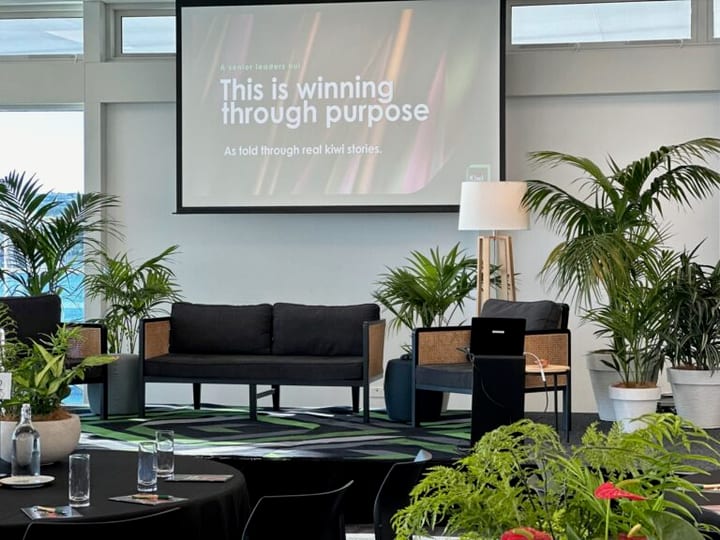 Function room set for a conference with projection screen, sofa seating area, and potted plants