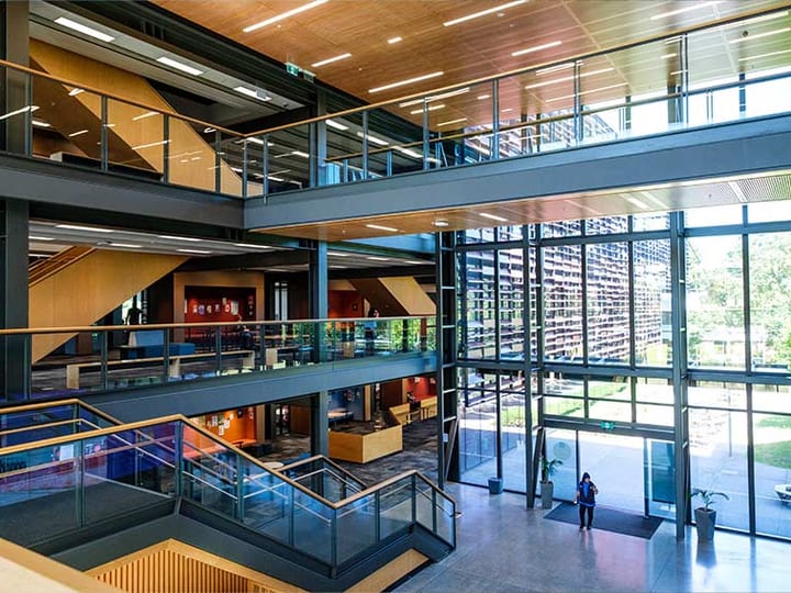 Multi-level building atrium with glass balustrades, timber ceiling panels, and full-height windows
