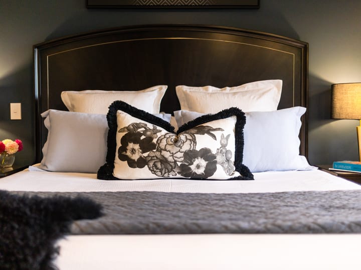 Dark-upholstered bed with floral cushion and bedside lamps, green-walled room