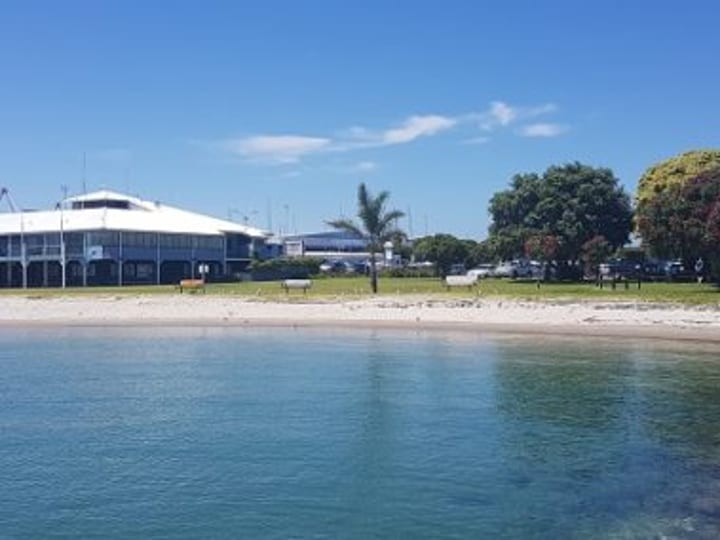 Club building viewed from water with beach and trees