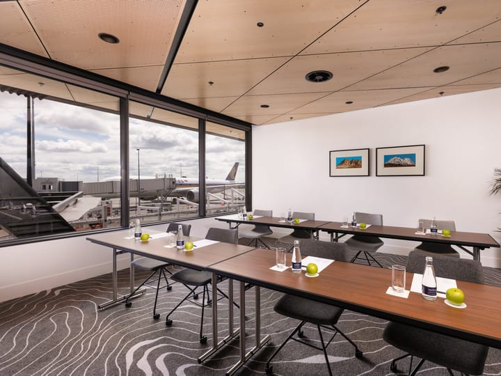 Small meeting room with timber ceiling, boardroom tables, grey chairs, and large window overlooking tarmac