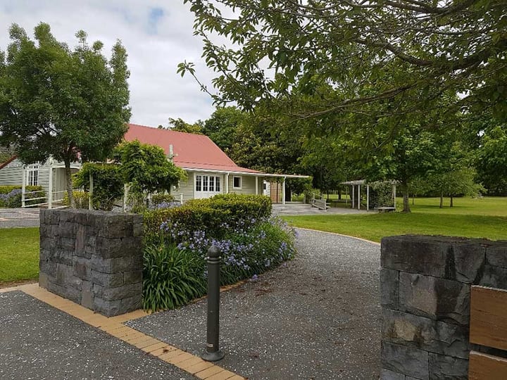 White weatherboard hall with red roof set in a green park with a pergola