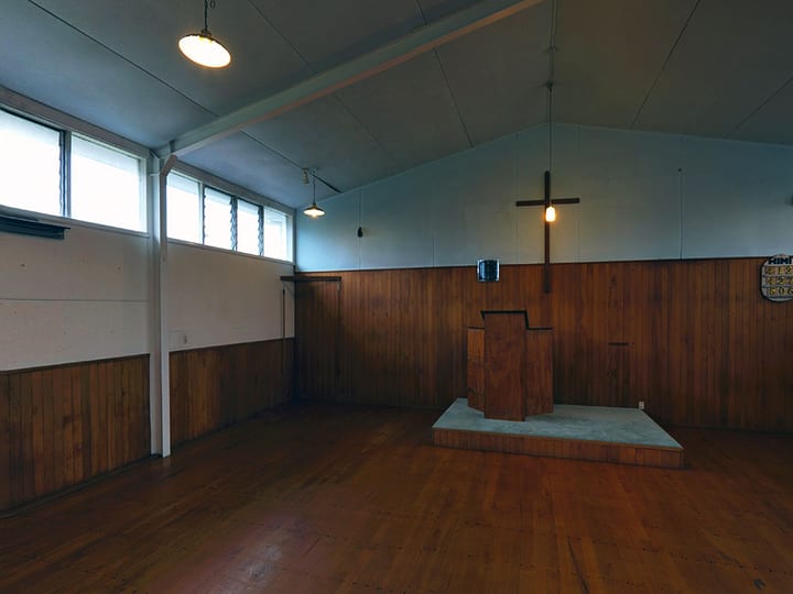Hall interior with timber walls, raised platform, and cross on wall