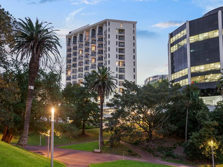 Tall white hotel tower with arched windows, seen from a park with tall trees at dusk