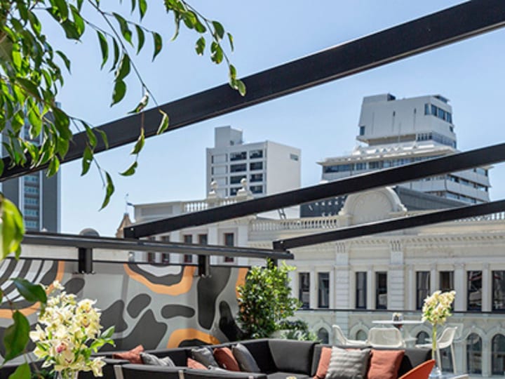 Rooftop terrace with dark sofas, orange chairs, geometric mural, and city buildings in background