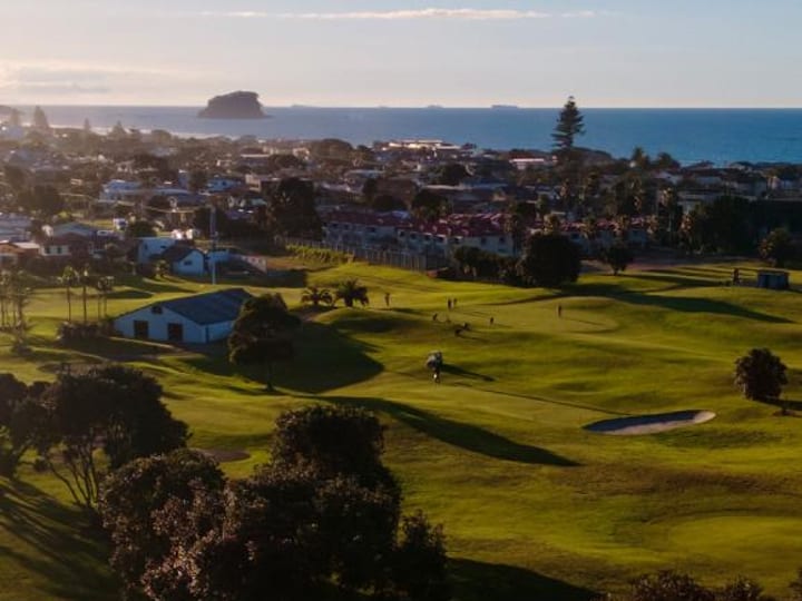 Aerial view of golf course fairways with coastal town and sea beyond