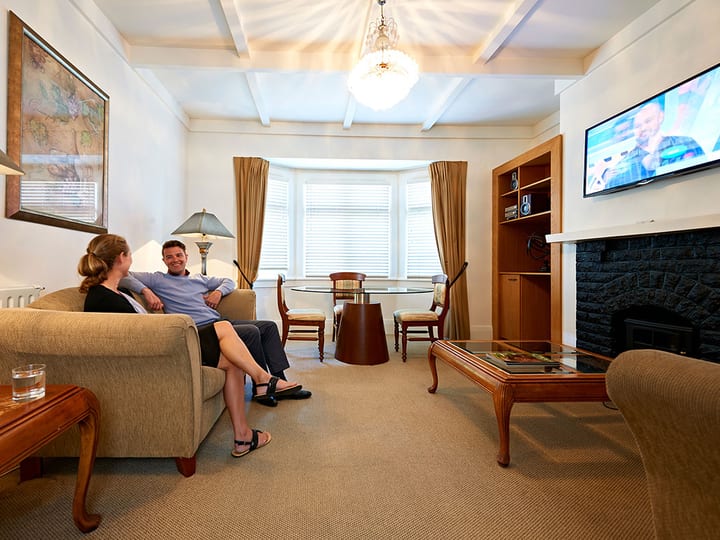 Suite sitting room with coffered ceiling, bay window, fireplace, timber furniture and neutral tones