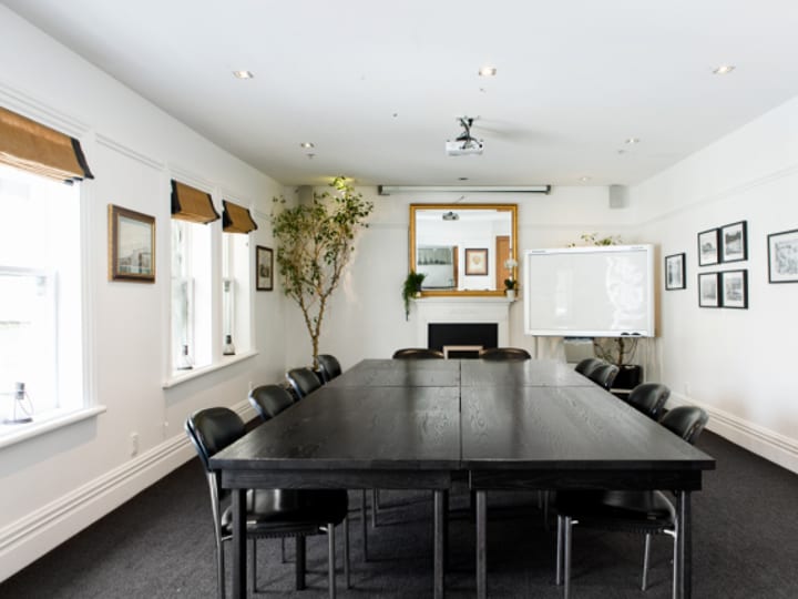 White-walled meeting room with long dark table, black chairs, fireplace and framed prints