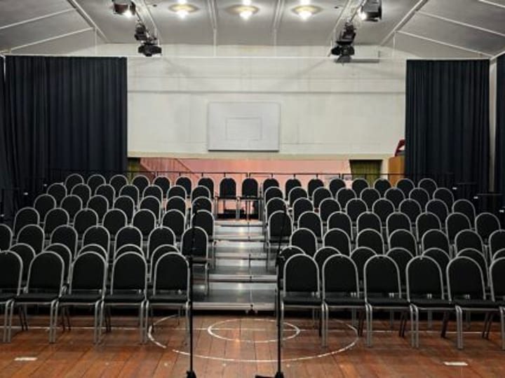Hall seating configured in rows facing a raised platform with screen and drapes