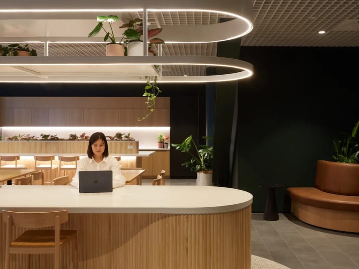 Contemporary open-plan workspace with curved timber reception counter, oval pendant lights, and hanging plants