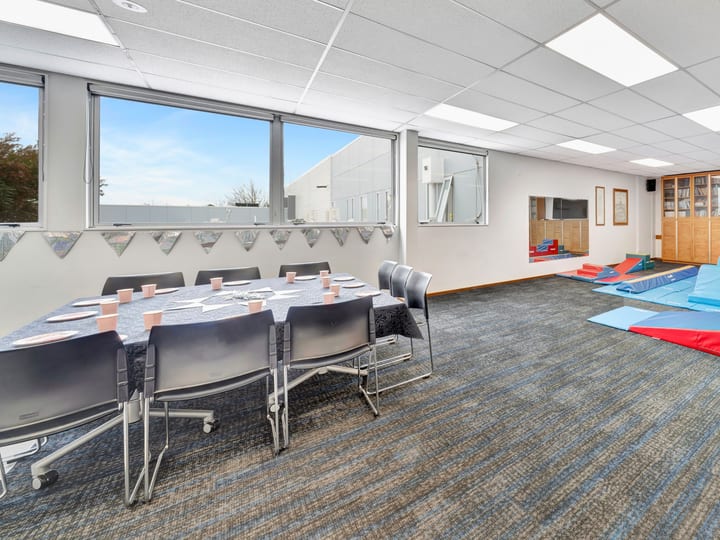 Carpeted activity room with round table, chairs and foam play equipment beside windows
