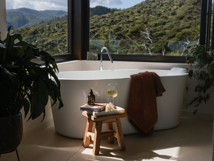 Freestanding bathtub beside large windows overlooking bush-covered hills