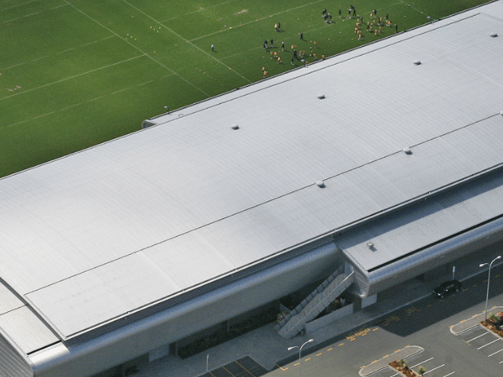 Aerial view of large indoor arena building with surrounding sports fields and car park