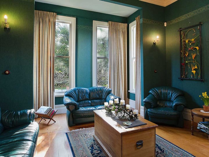 Sitting room with deep green walls, leather sofas, timber floor and tall sash windows