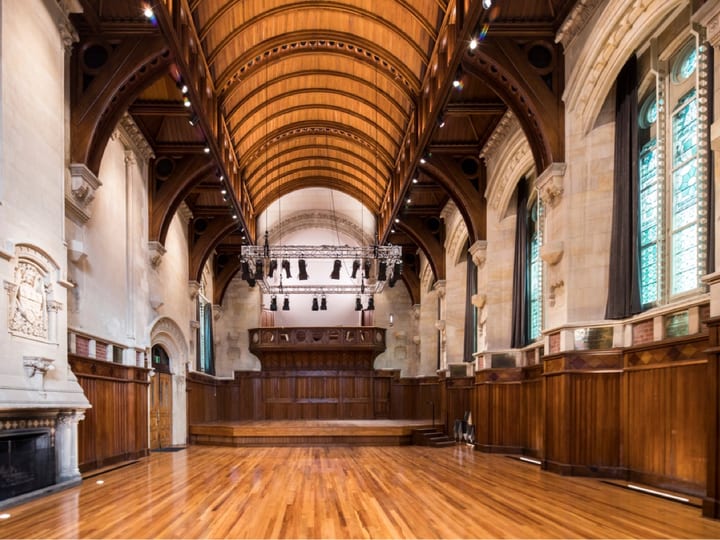 Grand hall with vaulted timber ceiling, stone arches, raised platform and polished floor
