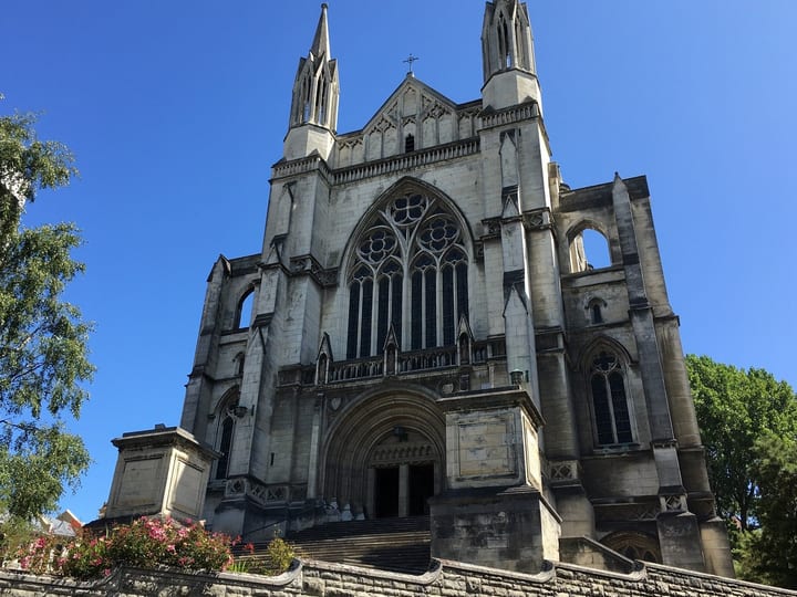 Large Gothic stone cathedral exterior with twin spires, rose window, grand entrance steps