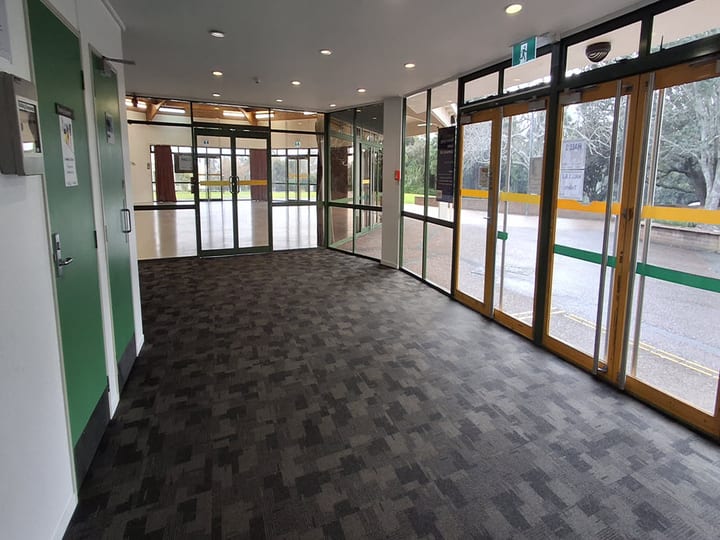Interior foyer with dark tile carpet, full-height glazing to car park, and green door