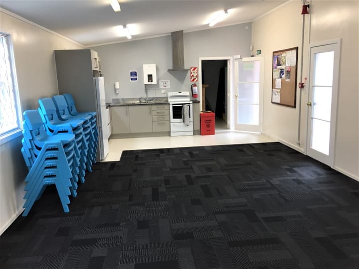 Open hall room with stacked blue chairs and kitchenette along one wall
